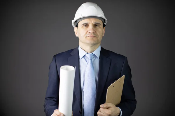 confident and calm builder in white helmet holds rolled-up drawing and clipboard