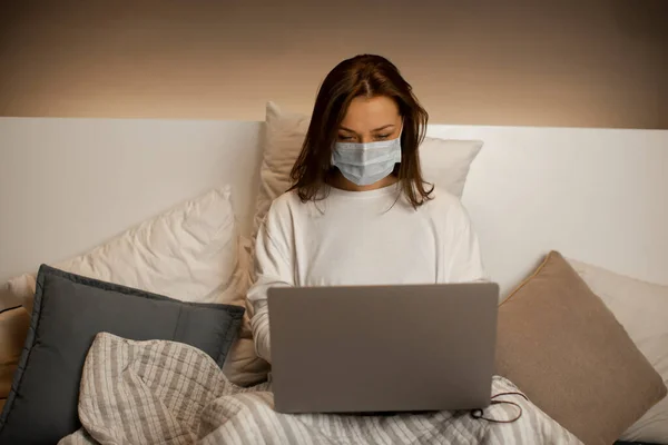 Joven mujer de negocios en médico sentado en la cama, trabajando en el ordenador desde casa — Foto de Stock