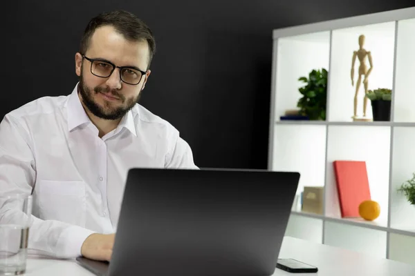 Joven hombre de negocios guapo trabaja en la computadora en la oficina del hogar. Freelancer sonriente — Foto de Stock