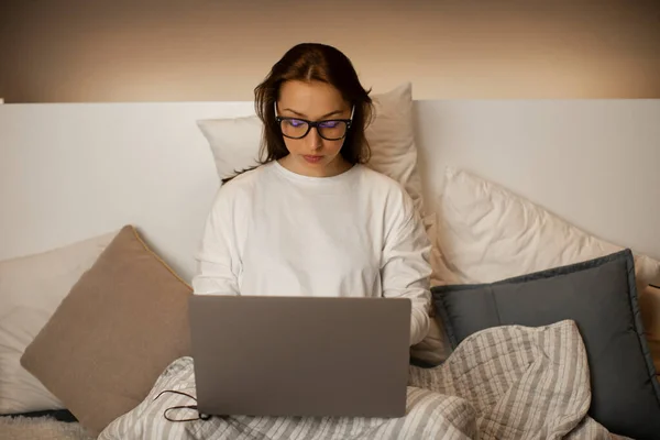Hermosa mujer de negocios sexy en gafas se sienta en la cama con el ordenador portátil, trabaja en casa — Foto de Stock