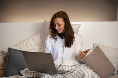 Güzel çoklu görev yapan serbest çalışan internetten iletişim kuruyor, laptopun başında yatakta çalışıyor.