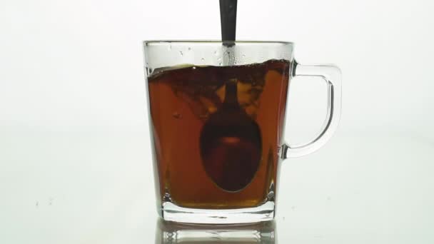 Κουτάλι αναδεύει το τσάι σε διαφανές γυάλινο κύπελλο δημιουργώντας δίνη, σωματίδια ζάχαρης γυρίζοντας τσάι. αργή κίνηση απομονωμένη σε λευκό φόντο από κοντά — Αρχείο Βίντεο