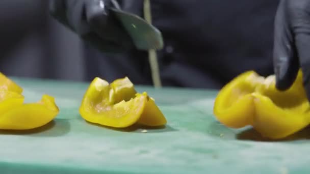 Cocina las manos en guantes negros picando pimientos amarillos de cerca — Vídeos de Stock