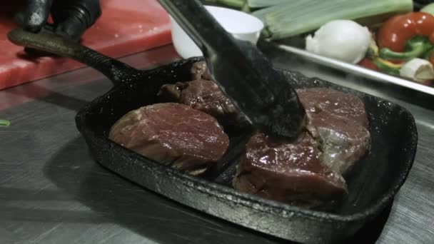 Повар переворачивает жареные говяжьи стейки в сковороде приготовления пищи с паром и дымом близко — стоковое видео