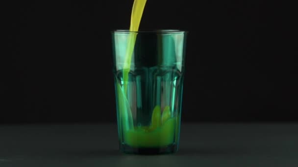 黒の背景のスローモーションで隔離された緑の多面的なガラスに注ぐジュース — ストック動画
