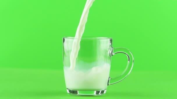 Leche vertiendo en taza de vidrio de cerca aislado sobre fondo verde claro cámara lenta — Vídeos de Stock