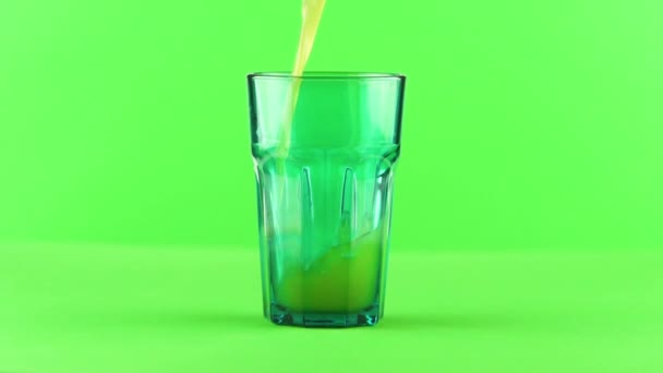Сок наливается в зеленое огранённое стекло, изолированное на светло-зеленом фоне замедленного движения — стоковое видео