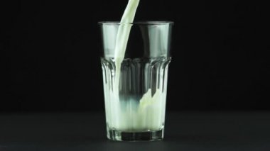 Süt katmanlı cama dökülüyor. Siyah arkaplanda izole edilmiş. Yavaş çekim.