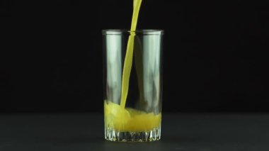 Meyve suyu, siyah arka planda ağır çekimde izole edilmiş bir şekilde cama dökülüyor.