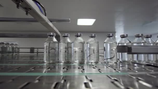 Garrafas de vidro preenchidas e seladas com tampas de borracha e alumínio na linha de transporte de solução médica — Vídeo de Stock