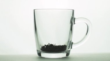 Siyah çay parçacıkları bardağa dökülüyor şeffaf bardağa ve çay demlemek için kaynar su ekleniyor beyaz arka planda izole edilmiş yavaş çekim yakın çekim