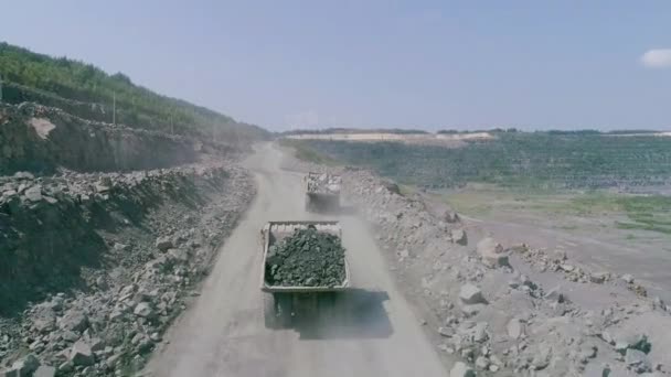 Mikashevichi, Belarus, 14.04.2020 - Mining dump trucks in large granite open pit mines.载货卡车在公路采石场边行驶无人驾驶飞机追逐高角度 — 图库视频影像