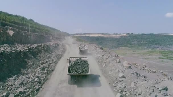 Mikashevichi, Bielorussia, 14.04.2020 - Autocarri con cassone ribaltabile in una grande miniera a cielo aperto di granito. Caricato camion corse su strada cava sporgenza drone inseguimento alto angolo — Video Stock