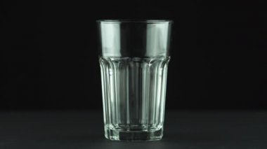 Süt, siyah arkaplanda izole bir şekilde cam parçalarına dökülüyor.