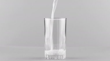 Açık gri arkaplanda izole edilmiş süt bardağa doluyor.