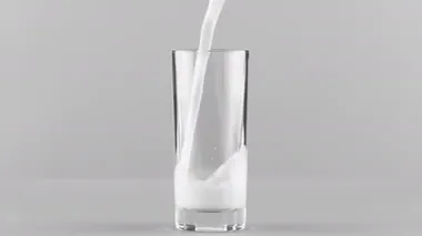 Açık gri arkaplanda izole edilmiş süt bardağa doluyor.