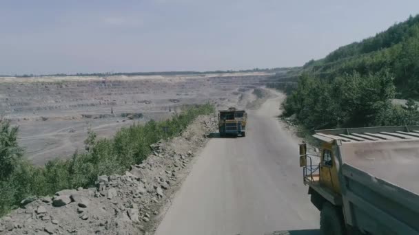 Camiones volquete mineros en gran mina de granito a cielo abierto. Cargado camiones paseos en carretera cantera repisa drone persecución vista superior de cerca de cámara lenta — Vídeo de stock