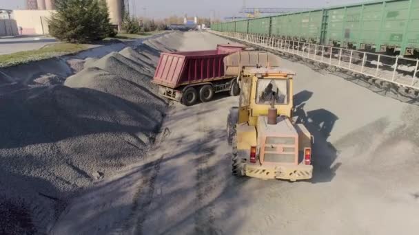 Cargador frontal carga grava en el cuerpo del camión de volteo en el centro logístico de la construcción — Vídeo de stock