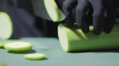 Elleri siyah eldivenlerle pişirir, kabakları keser seçici odaklanmayı kapatır.