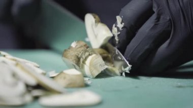 Elleri siyah eldivenle pişirir, mantarları keser.