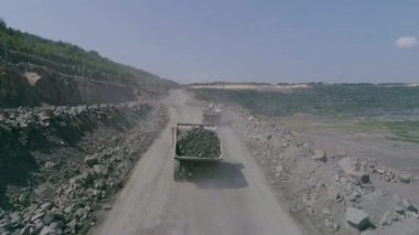 Büyük granit açık maden ocağında maden kamyonları. Dolu kamyon Quarry Road Drone 'a biniyor. Yüksek açılı ağır çekim kovalıyor.