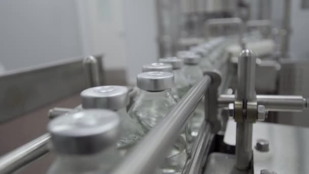 Скляні пляшки наповнені гумою та алюмінієвими кришками на лінії конвеєра медичного розчину крупним планом вибірковий фокус — стокове відео