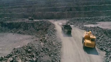 Büyük granit açık maden ocağında maden kamyonları. Yüklü kamyon taş ocağı çıkıntısı üzerinde uçuyor. İHA, hava aracı takip, yavaş çekim.