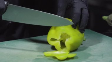 Elleri siyah eldivenle pişirir, biberleri keser seçici odağı kapatır.