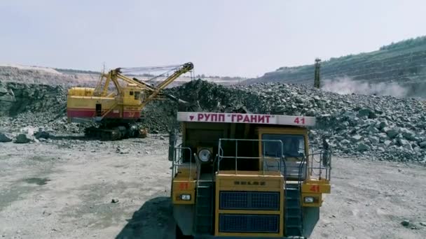 Mikashevichi, Bielorussia, 14.04.2020 - Grande escavatore carico granito in autocarro ribaltabile pesante Belaz rallentatore — Video Stock