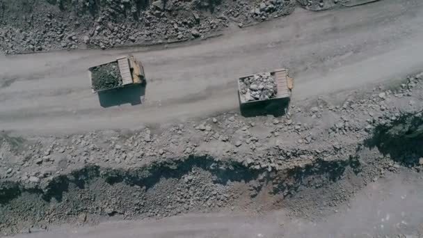 Mineração caminhões basculantes em granito grande mina poço aberto. Caminhão carregado passeios na estrada pedreira borda drone chase vista superior câmera lenta — Vídeo de Stock