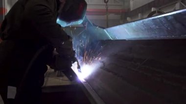 El yapımı metal kaynak, koyu arkaplanda kıvılcım akışı. Koruyucu maskeli kaynakçı