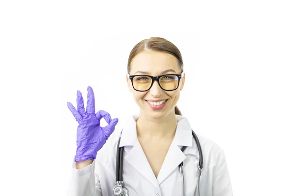 Χαμογελώντας γυναίκα γιατρός κοιτάζει κάμερα gesticulating εντάξει στο μπλε γάντι — Φωτογραφία Αρχείου