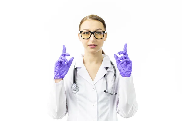 Jovem médico olha para a câmera apontando seus dedos indicadores em luvas azuis — Fotografia de Stock