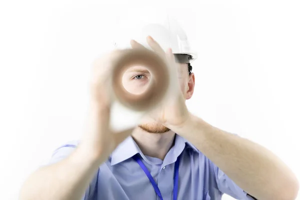 Engineer in safety helmet looks at camera through blueprint twisted into roll — Stock Photo, Image