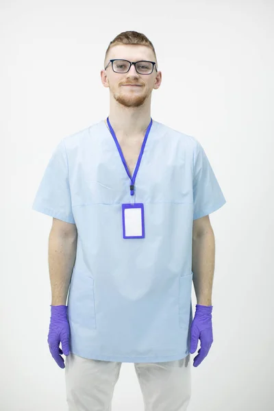 Jovem médico ou enfermeiro em óculos e luvas de borracha azul olha para a câmera — Fotografia de Stock