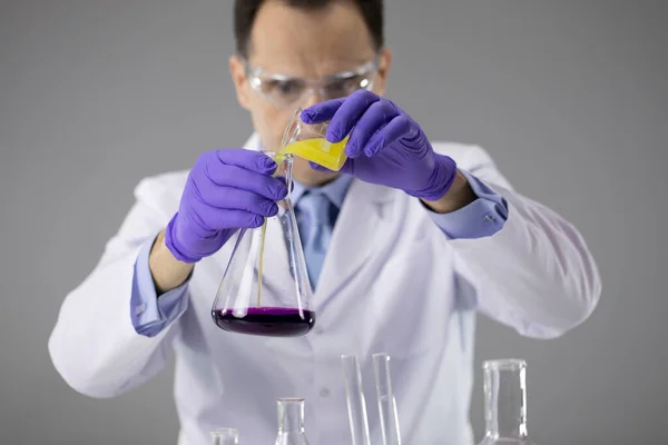 Chemicus onderzoeker in blauwe handschoenen en glazen gieten kleurrijke vloeistoffen in kolf — Stockfoto