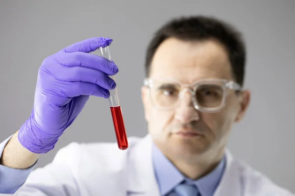 Mavi eldivenli kimyager elinde şeffaf kırmızı sıvıyla test tüpü tutuyor. — Stok fotoğraf