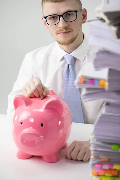 Atractivo hombre concentrado insertando moneda en la hucha en la oficina, finanzas — Foto de Stock