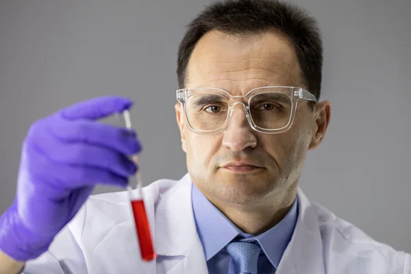 Крупный исследователь держит пробирку с красной жидкостью, синтезирующей новую вакцину — стоковое фото