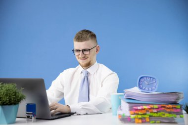 Erkek muhasebeci ofiste çalışıyor, gülümsüyor mavi dizüstü bilgisayar aksanına bakıyor.