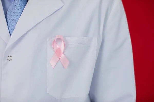 Medico quarantenne con nastro rosa. Concetto di consapevolezza del cancro su sfondo rosso — Foto Stock