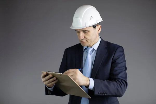 Hoofdingenieur in harde hoed maakt notities op klembord geïsoleerd op grijze achtergrond — Stockfoto