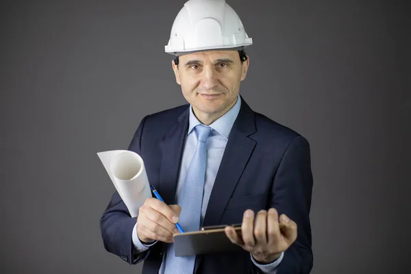 Confident engineer in hard hat with clipboard and blueprint roll looks at camera — Stock Photo, Image