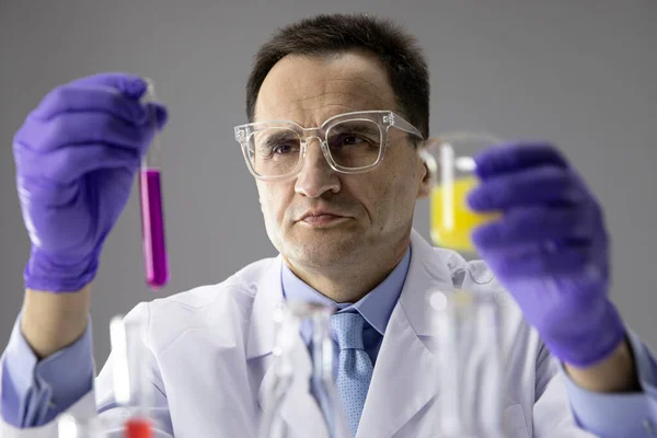 Мужчина-исследователь, работающий в химической лаборатории с реакционными трубками, проверяющий жидкости — стоковое фото