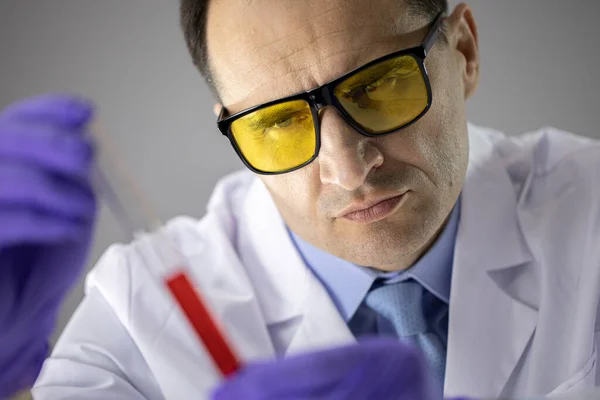 Közelkép tudós sárga védőszemüvegben elemző folyadék kémcsőben — Stock Fotó