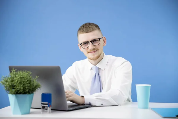 Gerente masculino en la oficina trabaja con portátil sonriente mira acento de la cámara en azul — Foto de Stock