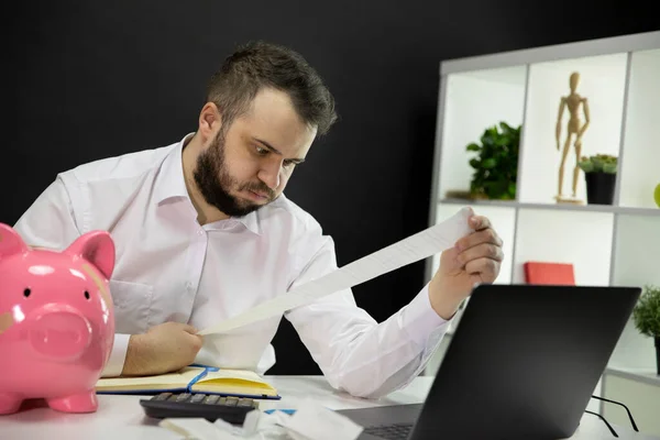 Frustrated business owner looking on long bills on his hands, broken piggybank