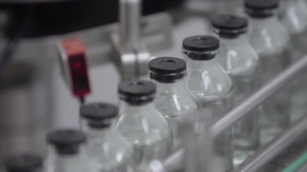 Botellas de vidrio llenadas y selladas con tapas de goma en una línea de transporte de soluciones médicas enfoque selectivo — Vídeo de stock