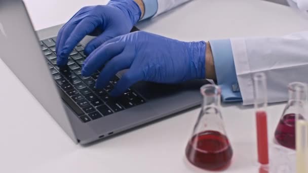 Chemik w rękawiczkach w laboratorium innowacji, piszący na laptopie. Zbliżenie — Wideo stockowe