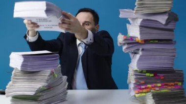 Orta yaşlı bir büro memuru masasındaki kağıtları değiştiriyor. İzole edilmiş mavi arkaplan.